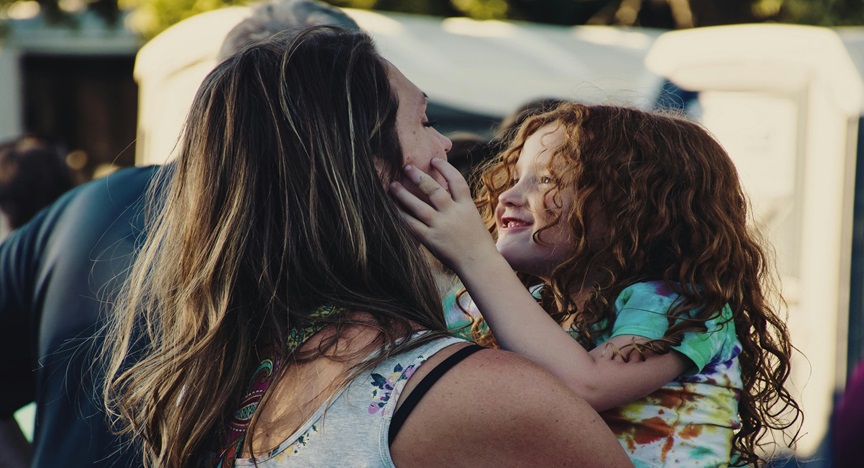 a mother holding her daughter outside at a fair day